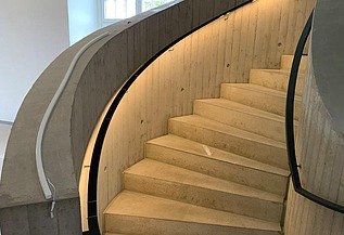 Geschwungene Betontreppe mit integrierter LED-Beleuchtung und moderner Elektroinstallation im Blockhaus Dresden – hochwertiger Innenausbau und Elektroarbeiten von SF‑Ausbau.