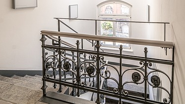 Saniertes Treppenhaus im Verwaltungsgebäude Hansastraße 13 in Dresden mit historischem Metallgeländer, Natursteinboden und modernisiertem Innenausbau – schlüsselfertige Sanierung durch SF‑Ausbau.