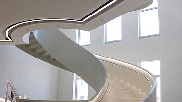 Geschwungene Designtreppe mit integrierter LED-Beleuchtung und hochwertiger Akustikdecke im Hörsaalzentrum der TU Bergakademie Freiberg – präziser Trockenbau und moderner Innenausbau von SF‑Ausbau.