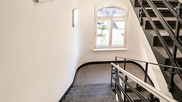 Saniertes Treppenhaus im Verwaltungsgebäude Hansastraße 17 in Dresden mit Natursteinstufen, historischen Geländern, großem Fenster und modernisiertem Innenausbau – schlüsselfertige Sanierung durch SF‑Ausbau.