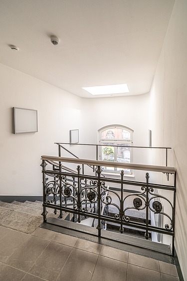 Saniertes Treppenhaus im Verwaltungsgebäude Hansastraße 13 in Dresden mit historischem Metallgeländer, Natursteinboden und modernisiertem Innenausbau – schlüsselfertige Sanierung durch SF‑Ausbau.