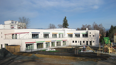 Moderne Kindertageseinrichtung in Freiberg mit großzügigen Spielbereichen, farbigen Fassadenelementen und Außenanlagen – Baustelleneinrichtung und Rohbau durch SF‑Ausbau.