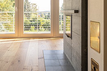 Moderner Wohnbereich mit Kaminofen, Holzfußboden und großer Fensterfront – hochwertiger Innenausbau und Bodenbelagsarbeiten von SF‑Ausbau in Freiberg.