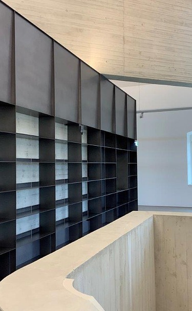 Modern ausgebauter Innenraum mit maßgefertigtem Regalsystem, Sichtbetonwänden, Holzdecke und offenem Galeriebereich im Blockhaus Dresden – hochwertiger Innenausbau und Elektroarbeiten von SF‑Ausbau.