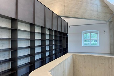 Modern ausgebauter Innenraum mit maßgefertigtem Regalsystem, Sichtbetonwänden, Holzdecke und offenem Galeriebereich im Blockhaus Dresden – hochwertiger Innenausbau und Elektroarbeiten von SF‑Ausbau.