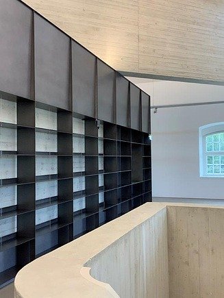 Modern ausgebauter Innenraum mit maßgefertigtem Regalsystem, Sichtbetonwänden, Holzdecke und offenem Galeriebereich im Blockhaus Dresden – hochwertiger Innenausbau und Elektroarbeiten von SF‑Ausbau.